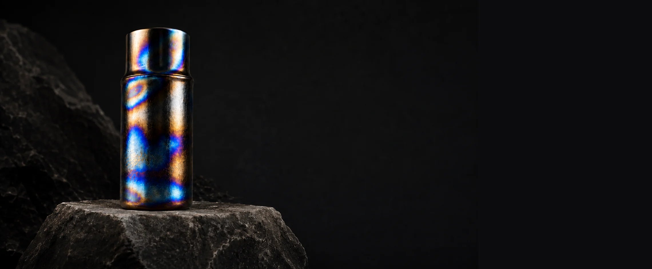 Blue, gold, and violet hand-fired titanium cup on a dark stone plinth